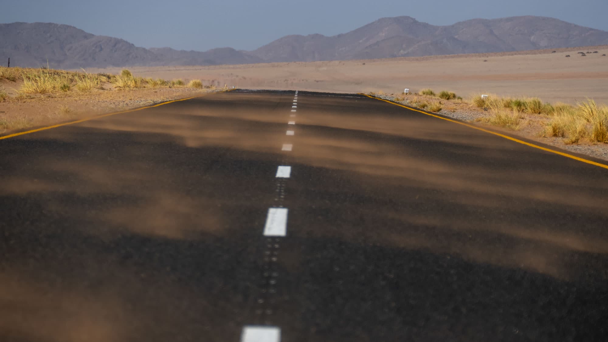 Die Straße nach Lüderitz führt schnurgerade durch Namibias kargen Süden - vor dir nur Asphalt, Wüste und die Berge am Horizont.