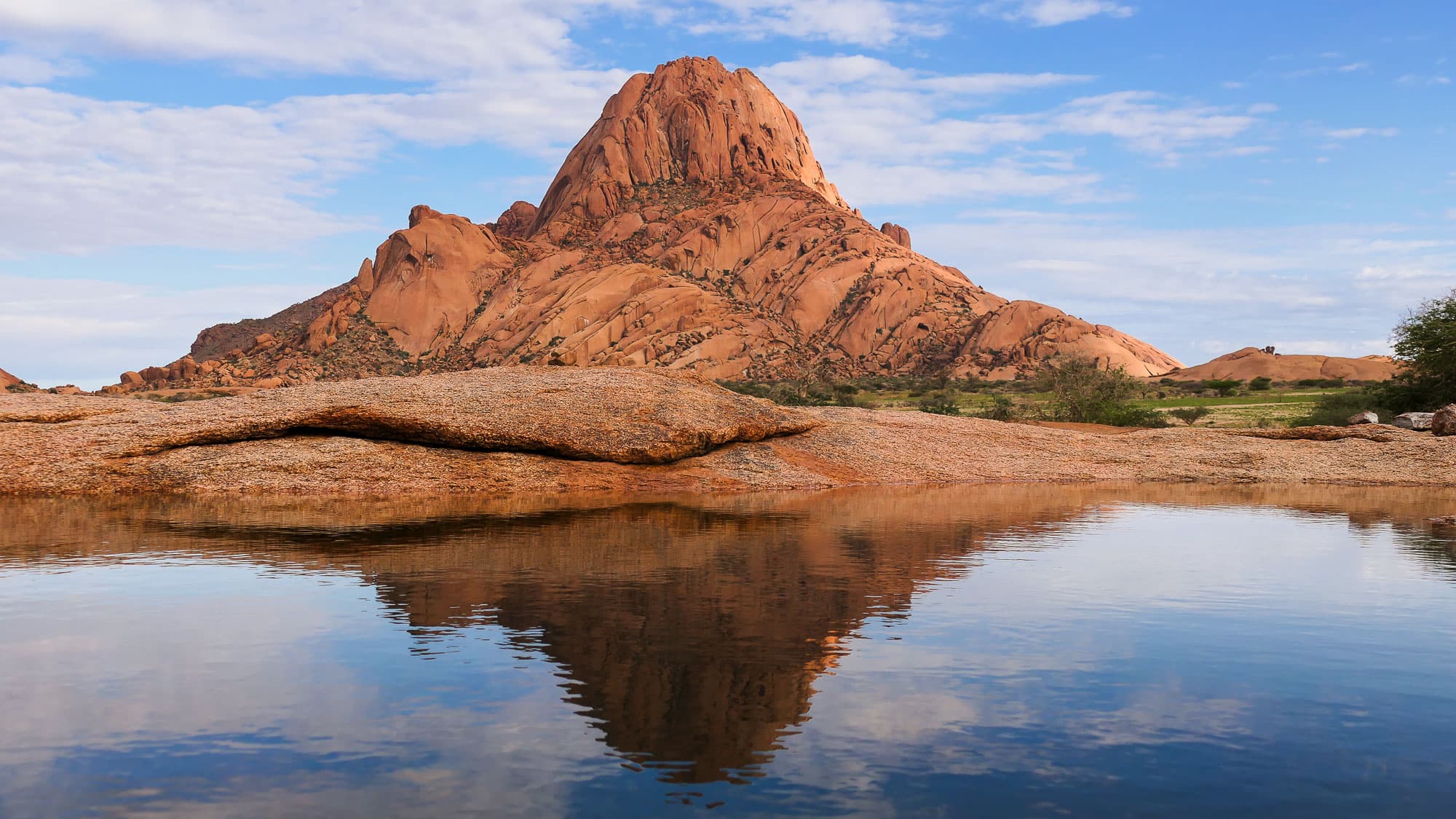 Nach dem Regen zeigt die Spitzkoppe ein seltenes Gesicht: Ihre mächtigen Granitfelsen spiegeln sich im Wasser eines natürlichen Felsenbeckens.